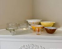 All Pyrex items arranged on shelf: three mixing bowls, two casserole dishes with lids, rectangular baking dish, amber measuring cup