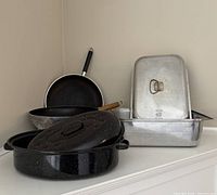 All four cookware items grouped: aluminum roaster, enamel oval roaster with lid, wok, frypan