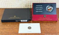 Outer black sleeve, red display card, coin in capsule, certificate visible