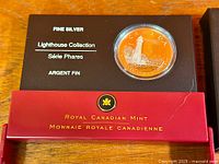 Coin in black display card within red outer sleeve, lighthouse design visible