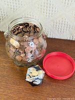 Jar filled with mixed pennies beside lid and lucite paperweight