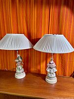 Pair of figural ceramic lamps with pleated shades on wood surface