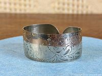 Angled view of sterling silver cuff showing floral engraving and monogram