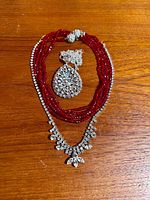All three jewelry pieces laid out: rhinestone necklace, red bead necklace, teardrop pendant