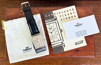 Watch, pouch, certificate booklet and guarantee card laid out on surface