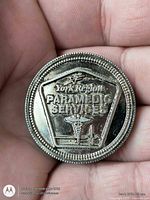 Front of silver-tone paramedic services challenge coin in hand