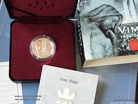 Coin in open presentation case beside outer box and certificate