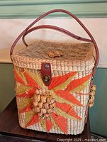 Front view of rectangular woven straw basket with leather handles and raffia decoration