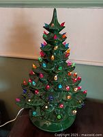 Full view of lighted green ceramic Christmas tree on base