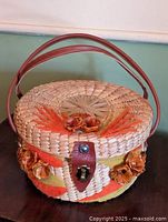 Top view of round woven straw basket with leather handle, latch, and raffia decorations