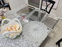 All items on countertop: frosted glass platter, clear glass bowl, ceramic basket bowl with shells, three metal trays