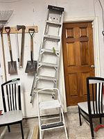 Full view of ladder leaning against wall with step stool in front