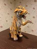 Front view of seated ceramic tiger with raised paw