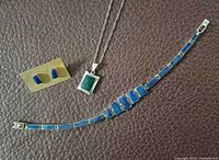 Bracelet, necklace with green pendant, pair of blue stone earrings displayed on brown surface