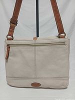 Rear view showing off-white pebbled leather body, exterior zip pocket, tan leather strap attachments