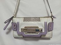 Front view of Guess faux croco crossbody clutch showing white, grey, lavender panels, front logo plaque and studs