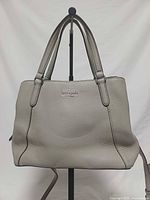 Front view of light grey Kate Spade satchel showing handles, logo, shape and piping