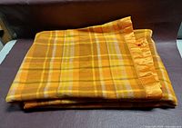 Folded yellow plaid wool blanket showing satin edge