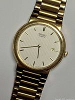 Close-up of watch dial, showing Seiko branding, date window, gold tone markers and hands