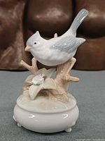 Front view of porcelain bird music box showing bird, branch, lily flower and base