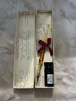 Open box showing amber glass dip pen and black ink bottle