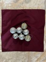 Seven assorted silver-tone ornament balls arranged on burgundy cloth