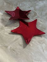 Two glossy metallic red star plates on fabric surface