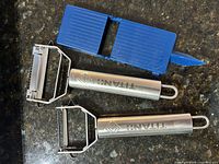 Two Titan stainless steel peelers and blue plastic corer on countertop