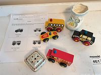 Group shot of four wooden vehicles, tin box, ceramic shoe with reference sheet