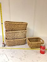 Stack of three large and one small matching woven baskets with measuring tape and soda can for scale