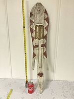 Full view of elongated carved wood mask beside measuring tape and soda can for scale