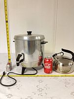 Full view of coffee urn with lid, spigot, power cord, kettle, measuring tapes and soda can for scale