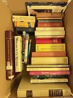 Box containing assorted books visible spines showing language dictionaries, cookbooks, pocket Bible and other titles