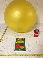 Yellow exercise ball on table with handbook and can for scale