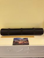 Black cylindrical storage bag with straps placed on shelf with ruler for scale