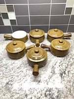 six brown handled soup bowls with lids displayed