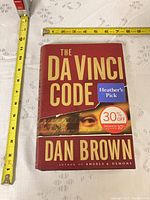 Front view of hardcover book showing title, author, stickers, and measuring tapes for scale