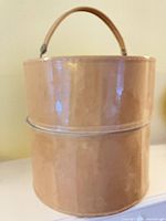Front view of beige cylindrical hat box with handle
