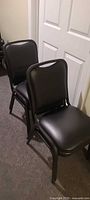 Side view of two black vinyl stacking chairs showing upholstery and frame