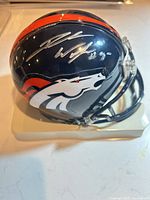 Left-front view of signed Broncos mini helmet on stand