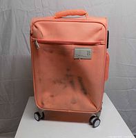 Front view of coral carry-on spinner showing exterior pocket, wheels and scuff marks