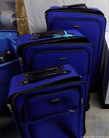 Three royal blue suitcases nested together showing fronts and carry handles