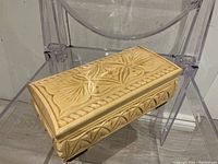Top angled view of carved blond wood box on clear chair