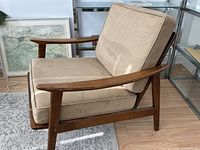 Side view of lounge chair showing curved wood arms, beige cushions, metal foot cap visible