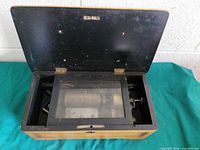 Music box open showing wood case, black interior lid and glass-covered movement