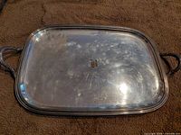 Top view of rectangular metal tray showing central monogram and handles