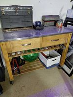 Overall view of rolling pine workbench with metal top, toolbox and items on shelves