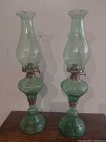 Full view of both green hurricane lamps on table