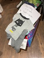 Box of boys 0-12 month clothing with Batman bodysuit and grey pants visible