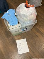 Overall view of plastic tote labeled Kids 0-?, clear bin and large bag containing clothing